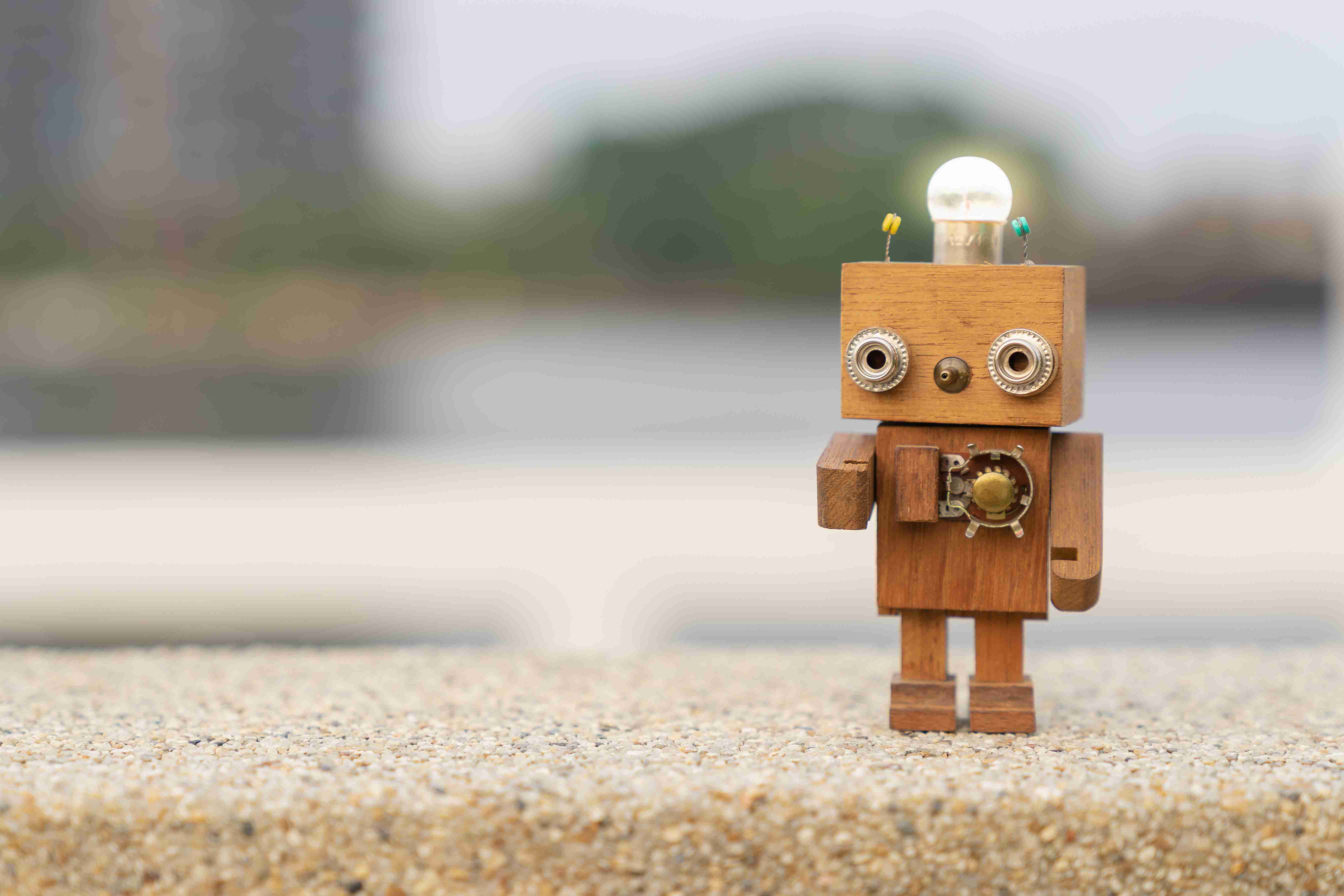 Mały drewniany robot w stylu retro z żarówką na głowie, stojący na stole.