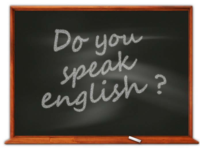Napis „Do you speak English?” zapisany białą kredą na czarnej tablicy szkolnej z drewnianą ramą.