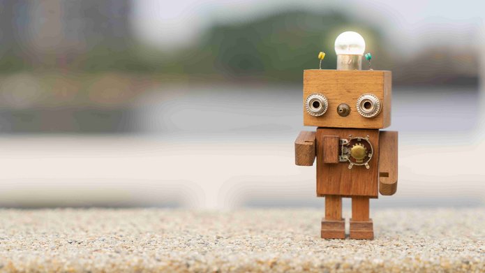 Little retro wood robot with light bulb on the head standing on the table.