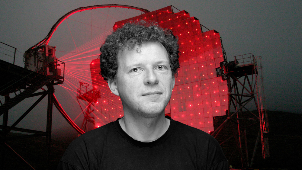Profesor Julian Sitarek na tle rozświetlonego czerwonymi laserami teleskopu czerenkowskiego