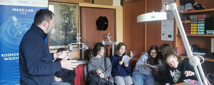 Uczniowie Szkoły Podstawowej nr 142 w Łodzi uczestniczą w zajęciach w laboratoriach Wydziału Fizyki i Informatyki Stosowanej Uniwersytetu Łódzkiego. Obserwują eksperymenty, mikroskopy i urządzenia do detekcji promieniowania kosmicznego, a prowadzący wyjaśniają zasady działania sprzętu i pokazują zastosowania fizyki w praktyce.